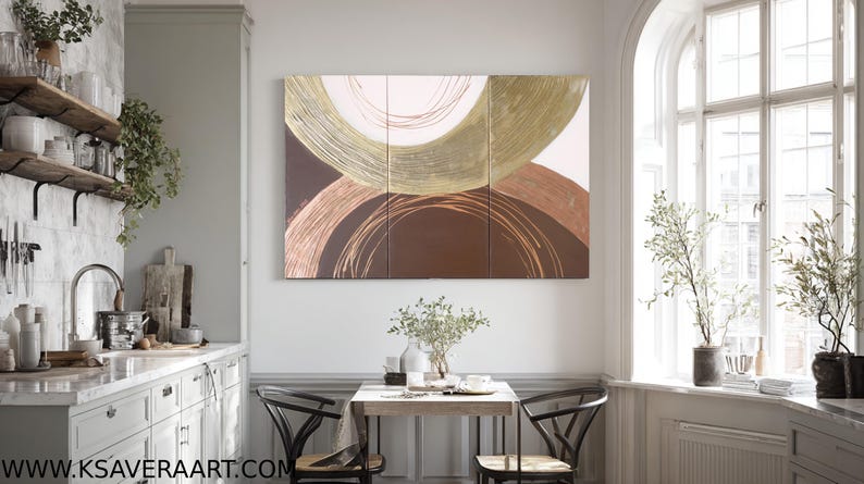 a modern kitchen with a large abstract painting hanging on the wall above a wooden dining table with two chairs. The kitchen is well-decorated with various plants and decorative items, creating a cozy and inviting atmosphere.