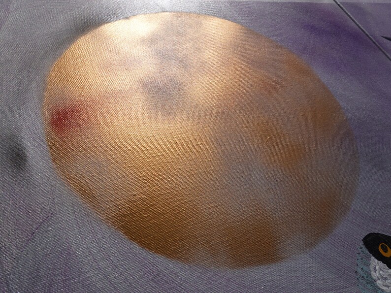 May include: A close-up of a gold-colored circle painted on a canvas background. The circle has a textured surface and appears to be a depiction of the moon.