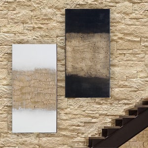 Peut inclure: Deux &oelig;uvres d'art murales rectangulaires abstraites. L'une est blanche avec une bande dor&eacute;e textur&eacute;e, l'autre est noire avec une bande dor&eacute;e textur&eacute;e. Les deux sont mont&eacute;es sur un mur de pierre brun clair.