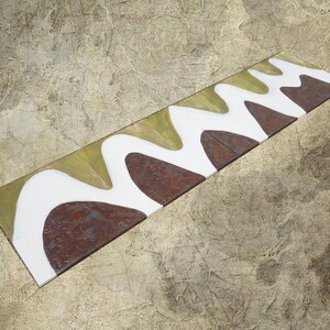 a long, rectangular piece of metal with a unique, abstract design in white and brown colors.