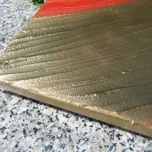 a close-up view of a metallic surface with a textured pattern, possibly gold or silver, and a red or orange stripe running across it.