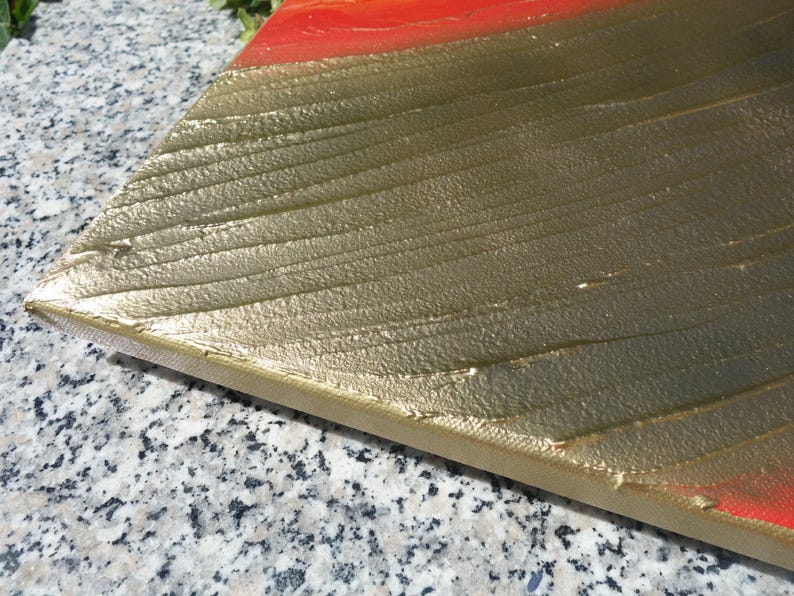 a close-up view of a metallic surface with a textured pattern, possibly gold or silver, and a red or orange stripe running across it.
