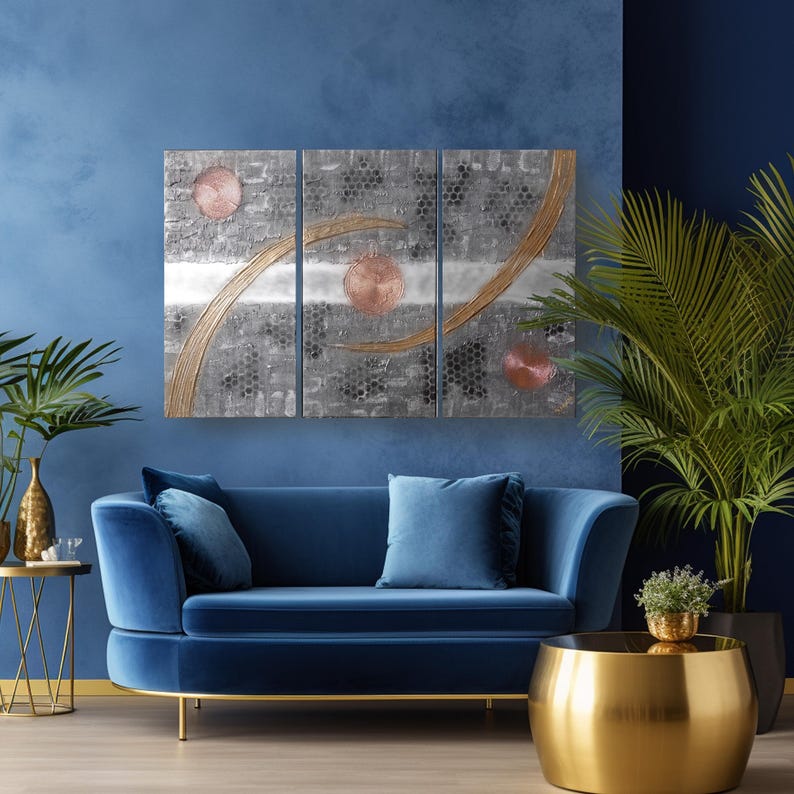 a modern living room with a blue velvet sofa, a gold round coffee table, and a large abstract painting on the wall.