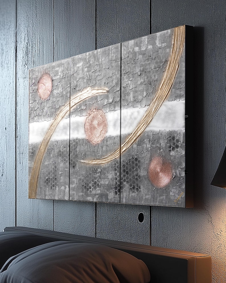 a modern art piece with a dark background and abstract design, including circles and lines, mounted on a wall above a bed.