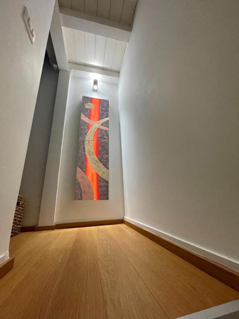 a hallway with a wooden floor and a large abstract painting hanging on the wall. The painting features a mix of orange and brown colors, creating a vibrant and dynamic visual effect. The hallway appears to be well-lit, with a light source visible in the top left corner.