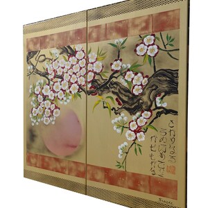 The image is a large painting depicting a branch with white flowers and a pink flower. The painting is framed with a gold border and has Japanese characters on the right side.