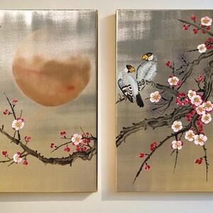 two paintings on a wall, depicting a large moon and cherry blossoms.