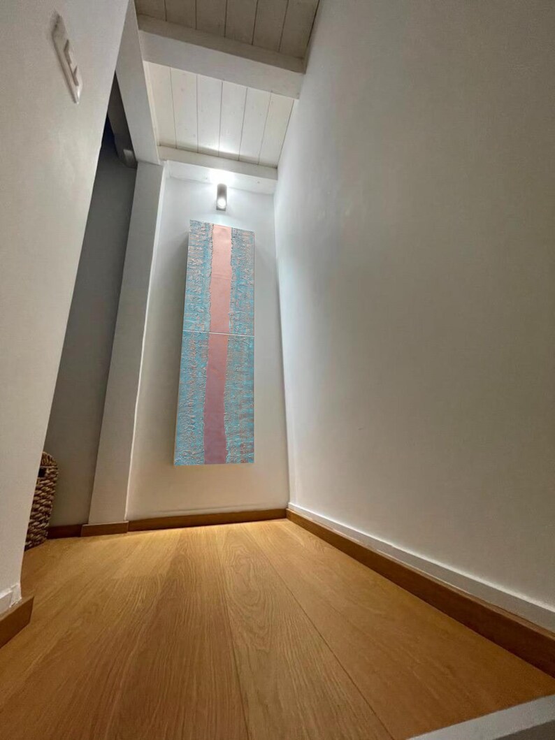 a hallway with a wooden floor and white walls. There is a large abstract painting hanging on the wall, which appears to be a colorful and textured piece. The hallway has a minimalist and clean design, with a single light source illuminating the space.