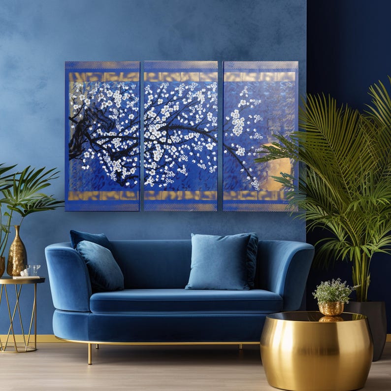 a living room with a blue velvet sofa, a gold round coffee table, and a large blue wall art depicting white flowers. The room is decorated with potted plants and gold accents, creating a luxurious and elegant atmosphere.