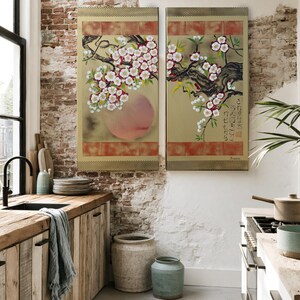 a cozy kitchen with a rustic wooden counter, a sink, and a large potted plant. The walls are adorned with two large paintings featuring floral designs, and the room is illuminated by natural light from the windows.