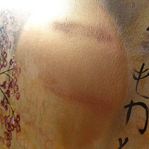 The image is a close-up of a textured surface with a golden hue, featuring a floral design and some Japanese characters.