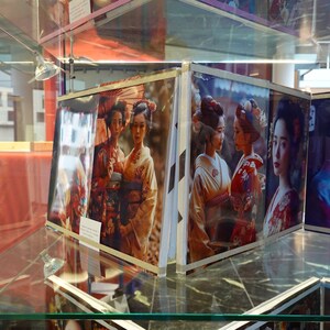 Puede incluir: Una vitrina que presenta varias fotograf&iacute;as enmarcadas de mujeres con kimonos japoneses tradicionales. Las im&aacute;genes muestran a las mujeres en varias poses, con patrones y colores detallados. La exhibici&oacute;n est&aacute; en un ambiente bien iluminado.