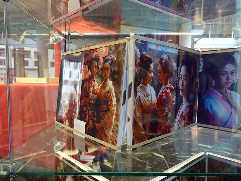 Puede incluir: Una vitrina que presenta varias fotograf&iacute;as enmarcadas de mujeres con kimonos japoneses tradicionales. Las im&aacute;genes muestran a las mujeres en varias poses, con patrones y colores detallados. La exhibici&oacute;n est&aacute; en un ambiente bien iluminado.