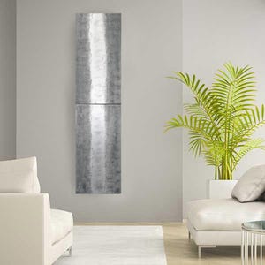 a modern living room with a minimalist design. The room features a white sofa, a white armchair, and a large potted plant. The walls are painted in a light gray color, and a large metal panel hangs on the wall.