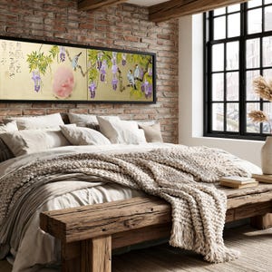 a cozy bedroom with a large bed, a wooden bench, and a brick wall with a framed painting of purple flowers hanging above it.