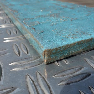 a close-up view of a blue metal surface with a textured pattern, resting on a metal plate with a diamond-like design.