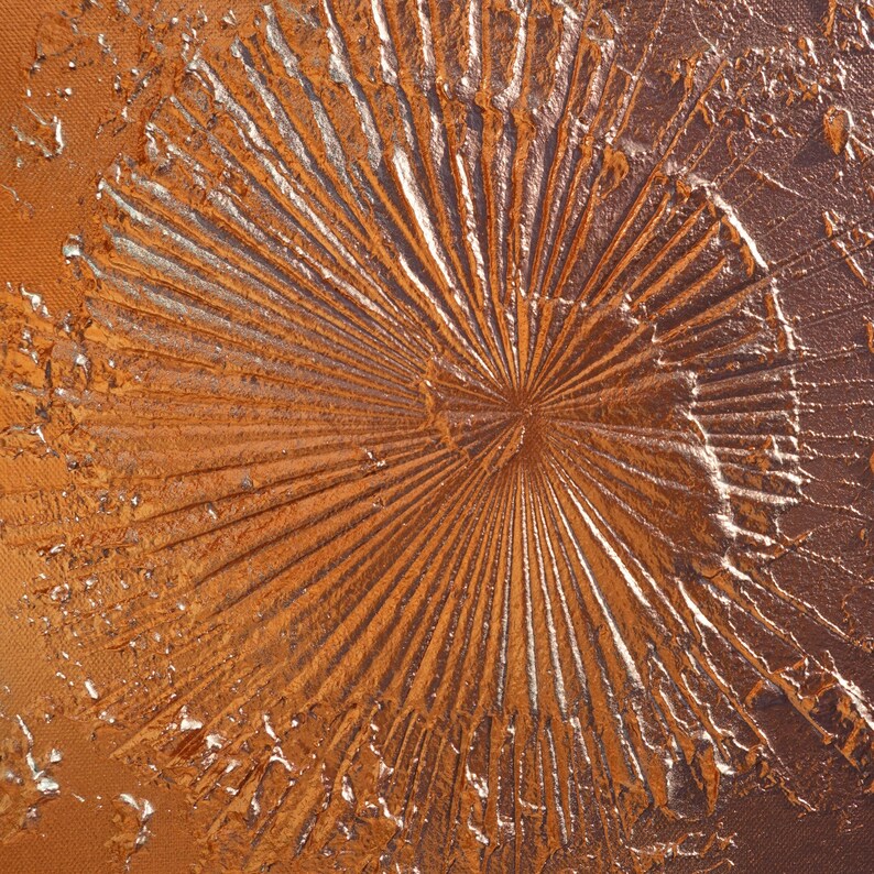 a close-up view of a textured surface with a metallic, metallic-looking appearance. The surface has a radial pattern, with lines radiating outwards from a central point, creating a sense of movement and dynamism. The overall color scheme of the image is a mix of orange and brown, with some areas appearing to be metallic or reflective.