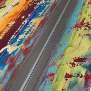 The image is a close-up of a vibrant, abstract painting with bold, colorful brushstrokes and splatters of paint. The painting features a mix of warm and cool colors, creating a dynamic and energetic visual experience.