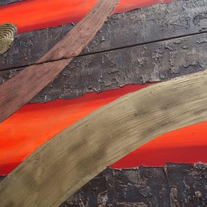 The image is a close-up of a textured surface with a striking contrast of red and black. The red appears to be a warm, fiery hue, while the black has a more muted tone. The surface has a rough, textured appearance, with a few cracks and chips visible. The image is a close-up of a wooden surface, possibly a piece of furniture or a wall, with a metallic or metallic-like texture.
