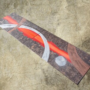 a piece of art with a striking abstract design. The artwork is composed of various shapes and colors, including red, white, and brown, creating a visually captivating composition.
