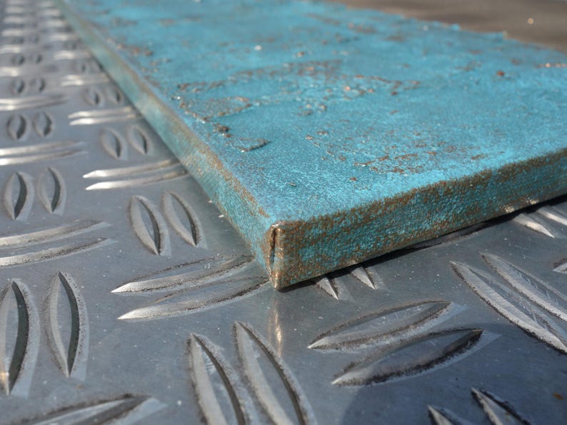 a close-up view of a blue metal surface with a textured pattern, resting on a metal plate with a diamond-like design.