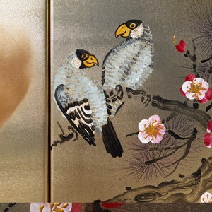 two birds perched on a branch with flowers, and there is a person's shadow on the left side of the frame.