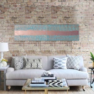 a modern living room with a gray sofa adorned with patterned throw pillows, a glass coffee table, and a brick wall backdrop. A large abstract painting is displayed above the sofa, adding an artistic touch to the space.