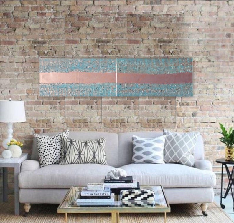 a modern living room with a gray sofa adorned with patterned throw pillows, a glass coffee table, and a brick wall backdrop. A large abstract painting is displayed above the sofa, adding an artistic touch to the space.