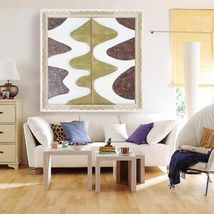 a modern living room with a white sofa, a white armchair, and a white coffee table. Above the sofa, there is a large abstract painting with a white and green color scheme. The room also features a white dresser, a lamp, and a window with yellow blinds.