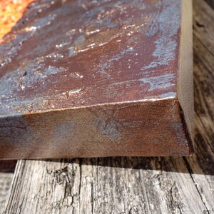a close-up view of a weathered, rusted metal surface, possibly a piece of furniture or a metal object, with a textured, worn appearance.