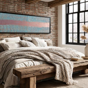 a cozy bedroom with a large bed, a wooden bench, and a brick wall with a large window. The bed is covered in white bedding and has a large blanket draped over it. The wooden bench is positioned next to the bed, and a vase is visible on the windowsill. The brick wall adds a rustic touch to the room, and a large window allows natural light to enter the space.