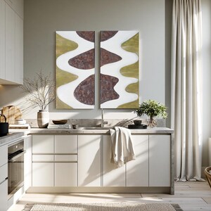 a modern, well-lit kitchen with white cabinets, a large abstract painting on the wall, and a dining table with chairs.