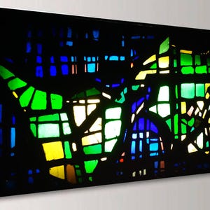 The image is a vibrant stained glass window with a colorful, abstract design composed of various geometric shapes and patterns in a range of green, blue, yellow, and orange hues.