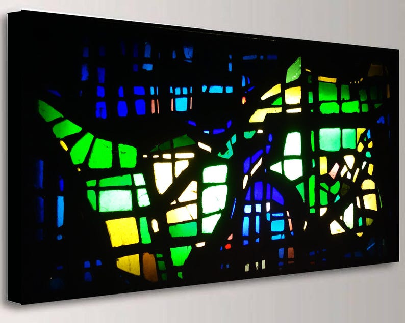 The image is a vibrant stained glass window with a colorful, abstract design composed of various geometric shapes and patterns in a range of green, blue, yellow, and orange hues.