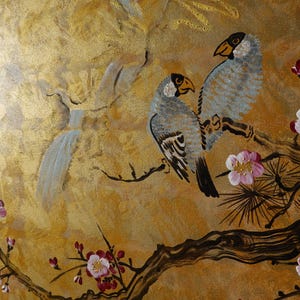 The image is a painting featuring two birds perched on a branch with pink and white flowers. The background is a golden color, and there is a bird flying in the background.