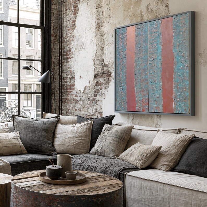 a cozy living room with a large window overlooking a cityscape. The room features a comfortable couch with a wooden coffee table in front of it, and a large abstract painting with vertical stripes in shades of blue and red hanging on the wall.