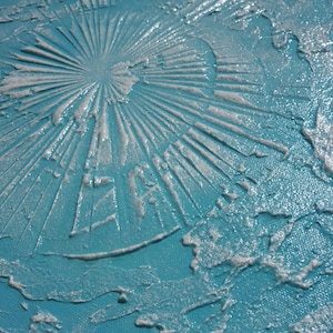 a close-up view of a textured surface with a blue-green hue, featuring a circular pattern or design created by a substance that appears to be a mixture of white and blue materials.