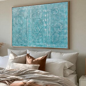 a large, three-panel artwork hanging on a wall above a bed with white pillows and a brown throw pillow.
