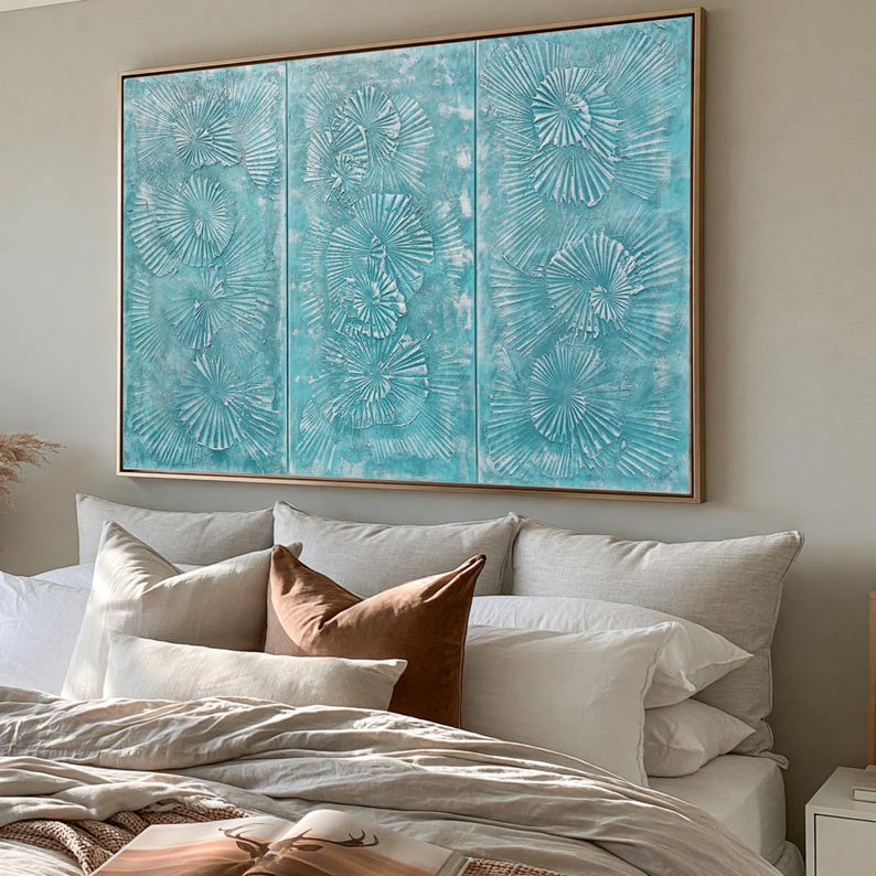 a large, three-panel artwork hanging on a wall above a bed with white pillows and a brown throw pillow.