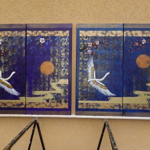 two paintings of white swans against a dark blue background, with a large orange moon and pink flowers in the center.