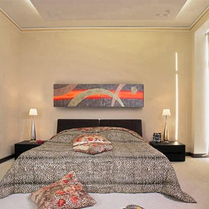 a modern bedroom with a large bed, a nightstand, and a painting on the wall. The room has a neutral color scheme with beige walls and a black and white patterned bedspread.
