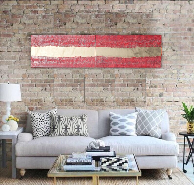 a modern living room with a gray sofa adorned with patterned throw pillows, a glass coffee table, and a brick wall backdrop. Above the sofa, there is a large, colorful abstract painting in red and white.