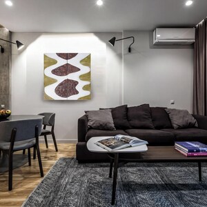 a modern living room with a black sofa, a wooden coffee table, and a dining table with chairs. The room has a minimalist and contemporary design, with a large abstract painting on the wall and a window with curtains.