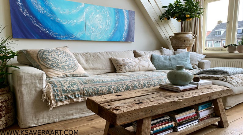 a cozy living room with a large window overlooking a cityscape. The room is furnished with a beige sofa, a wooden coffee table, and a large abstract painting on the wall. The room is decorated with various plants and books, creating a warm and inviting atmosphere.