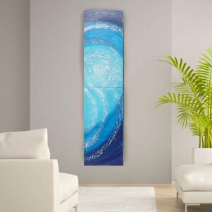 a modern living room with a large, colorful abstract painting hanging on the wall. The painting depicts a swirling pattern of blue and white colors, creating a sense of movement and energy. The room is furnished with a white sofa and a potted plant, adding to the contemporary and minimalist aesthetic.