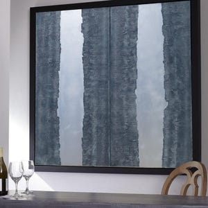 a large, square painting with vertical stripes in shades of blue and gray, hanging on a wall above a wooden table. There are two wine glasses on the table, and a bottle is visible on the left side of the table.