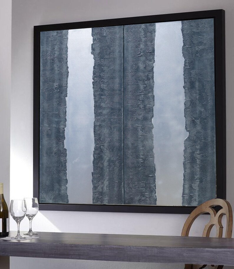 a large, square painting with vertical stripes in shades of blue and gray, hanging on a wall above a wooden table. There are two wine glasses on the table, and a bottle is visible on the left side of the table.