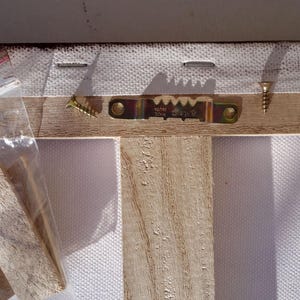 a wooden frame with a metal bracket attached to it, and a clear plastic bag containing a wooden block.