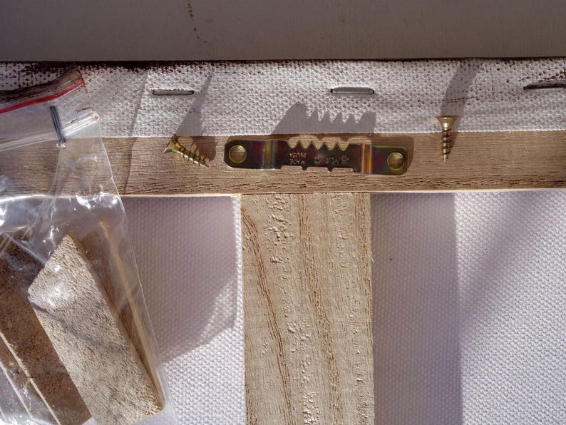 a wooden frame with a metal bracket attached to it, and a clear plastic bag containing a wooden block.