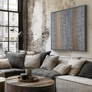 a cozy living room with a large window overlooking a cityscape. The room features a comfortable couch with a wooden coffee table in front of it, and a large abstract painting on the wall. The overall decor has a rustic and modern aesthetic, with a mix of neutral colors and natural textures.